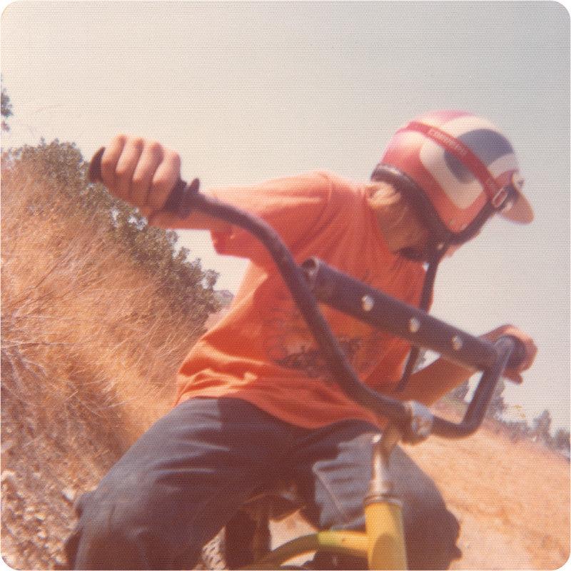 Vintage photo from the 70's of a young daredevil boy riding a bike and looking behind him