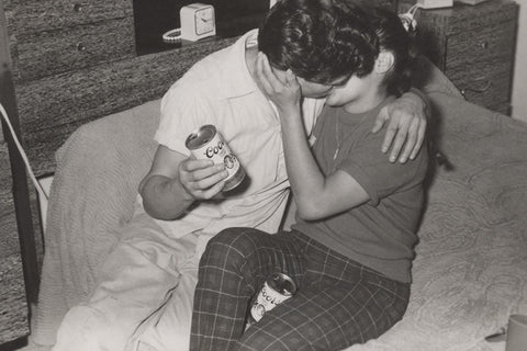 Black and white vintage photo of a young couple making out and holding Coors beer cans
