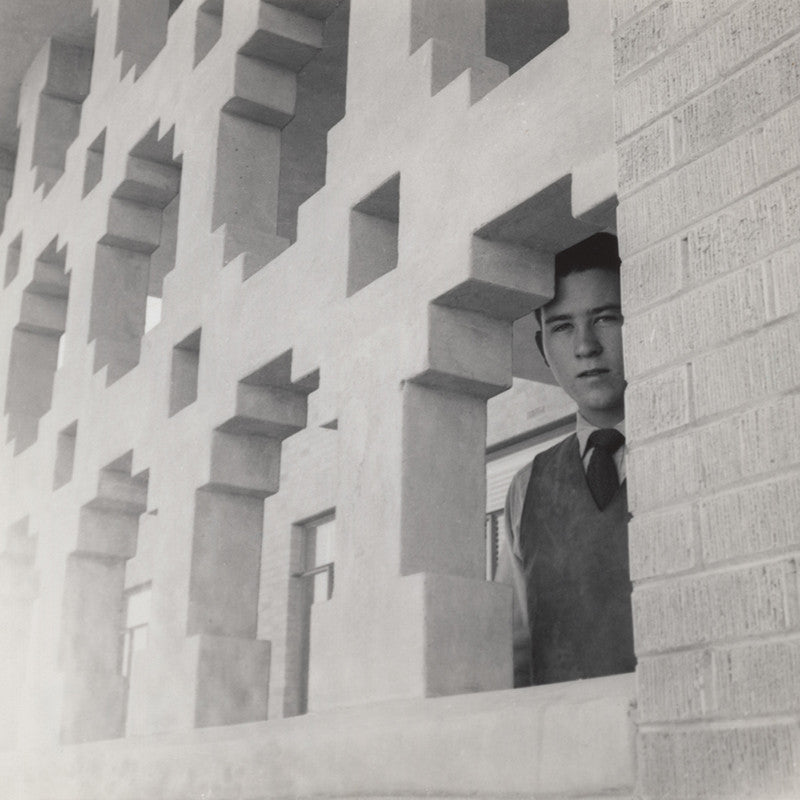 Black and white vintage photo of a young man peeking through an intricately designed wall