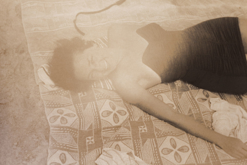 Sepia-toned vintage photograph of a beautiful young woman laying on the beach in a bathing suit