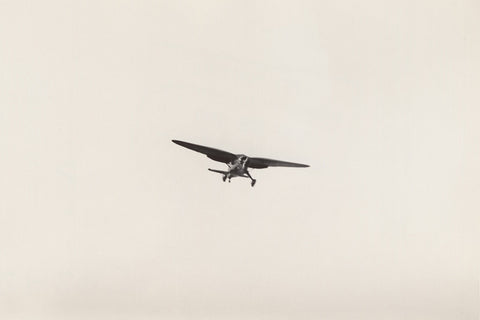 Cream-hued vintage photo of an airplane flying surrounded by empty sky