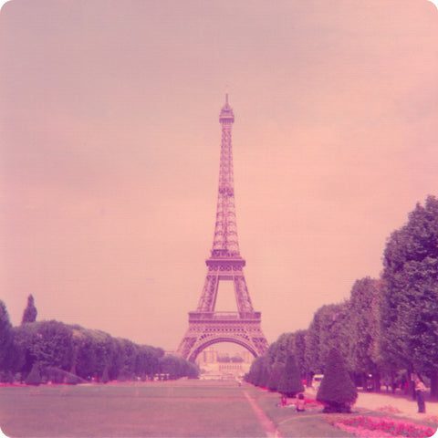 Pink hued square vintage photograph of the Eiffel Tower with the grounds and trees in the foreground