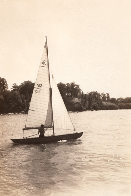Black and white vintage photograph of a small sailboat gliding through water