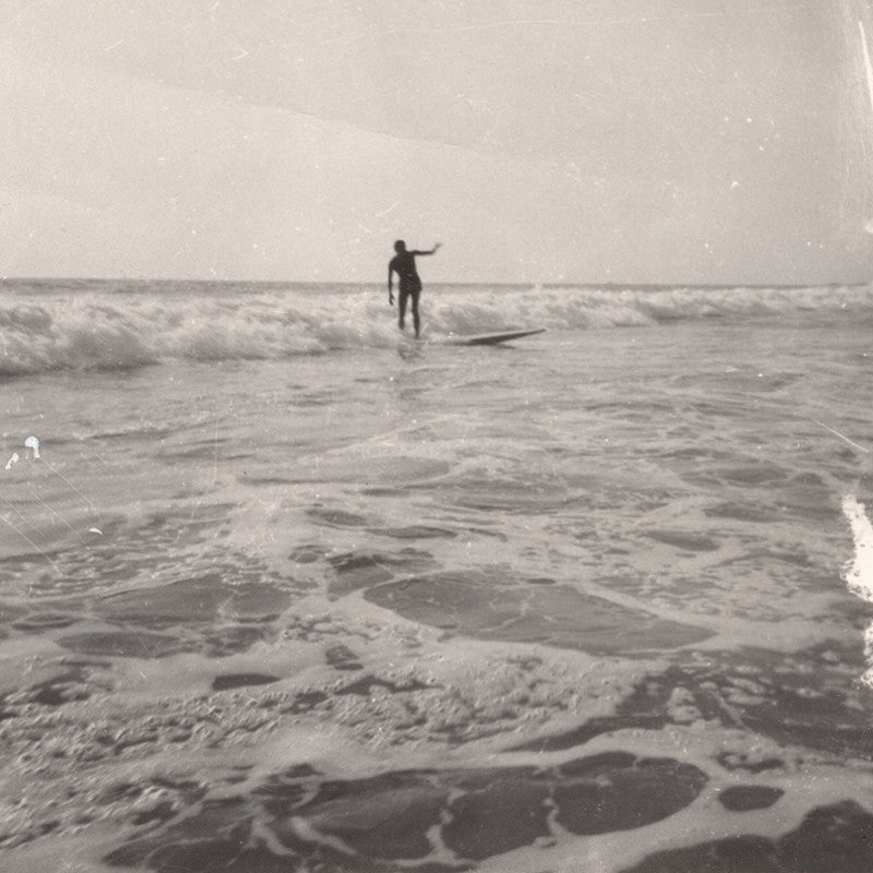 Black and white vintage photo of a surfer catching a wave in the background and foamy ocean water in the foreground