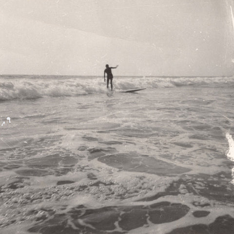 Black and white vintage photo of a surfer catching a wave in the background and foamy ocean water in the foreground