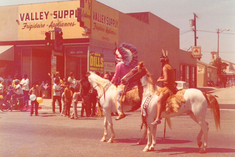 Vintage color photo of two Native Americans on horseback riding on the streets of a modern town 