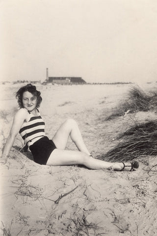 Black and white vintage photo of a beautiful young woman posing on a beach with her striped bathing suit