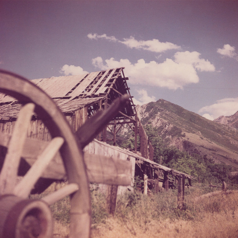 Vintage photo from the 70's of a wild west town with a wagon wheel in the foreground and an old barn in the background